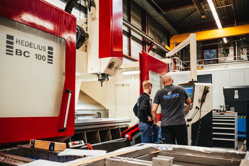 Twee mensen bedienen CNC-machine in werkplaats.